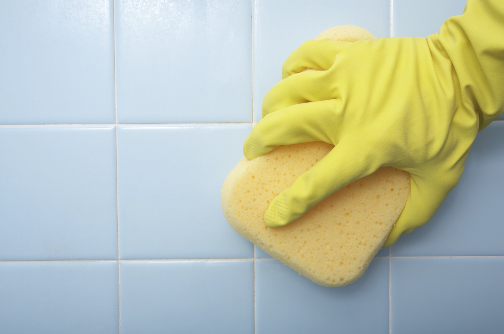 Rubber-gloved hand scrubbing bathroom tile with a sponge